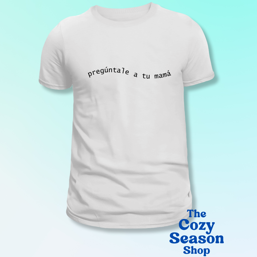 White crew neck t-shirt with text "PREGUNTALE A TU MAMA" on the front, from the brand 'The Cozy Season Shop'.