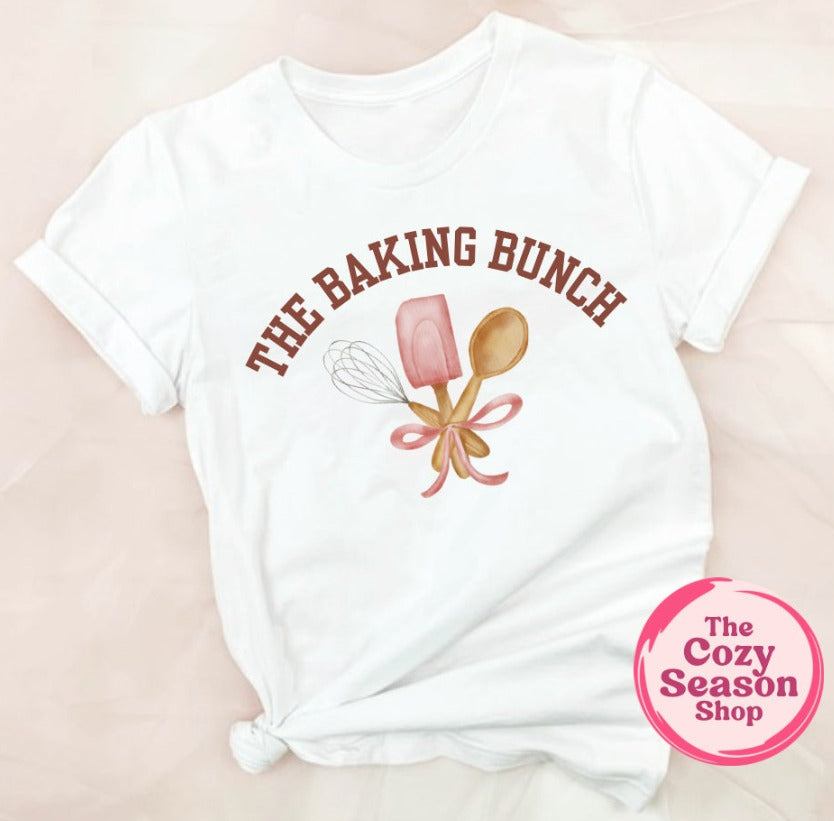 White t-shirt with 'The Baking Bunch' design and a pink logo on a beige background