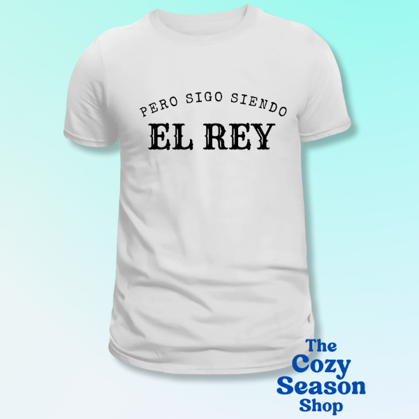 White t-shirt with black text 'Pero Sigo Siendo El Rey' on a light blue background, branded 'The Cozy Season Shop'.