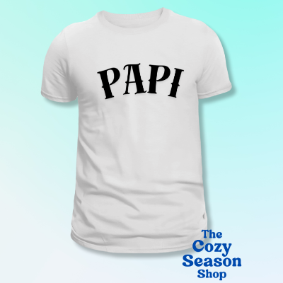 White t-shirt with 'PAPI' printed in black on a light blue background, featuring 'The Cozy Season Shop' logo.