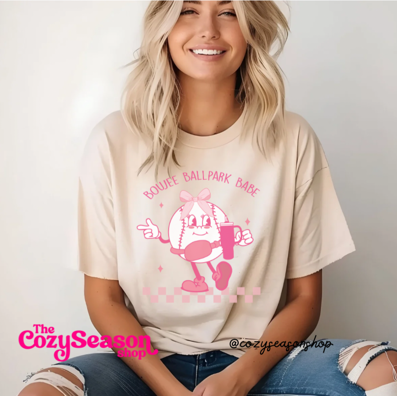 A woman wearing a beige t-shirt with a pink graphic of a cartoon character and the text 'ROUGE DE BASEBALL BABE', indicating support for a baseball team.