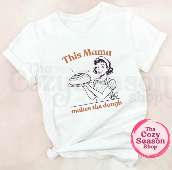 white tshirt with a pinup style woman holding a sourdough loaf. the text "this mama makes the dough" in orange text.