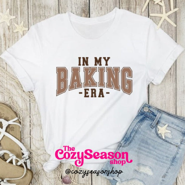 A white cotton t-shirt with the text 'IN MY BAKING ERA' printed in brown.