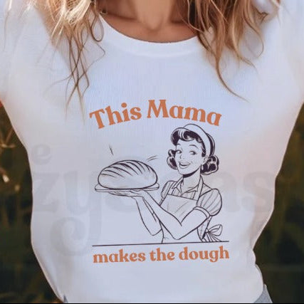 white tshirt with a pinup style woman holding a sourdough loaf. the text "this mama makes the dough" in orange text.
