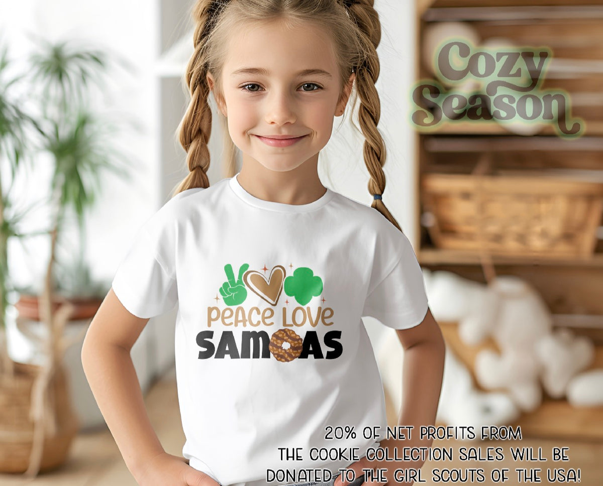 Young girl wearing a white t-shirt with 'Peace Love Samoas' design, standing in a cozy indoor setting.