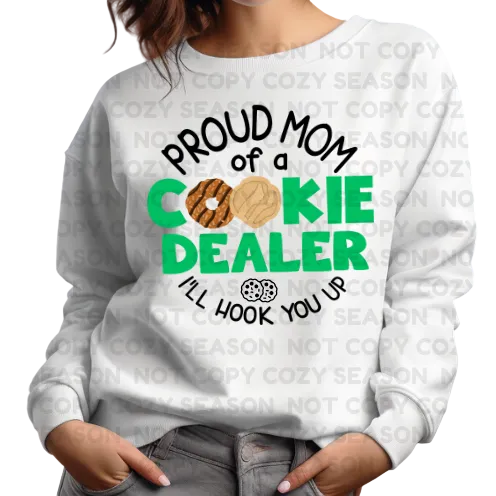 Person wearing a white sweatshirt with a humorous cookie-themed design. “Proud mom of a cookie dealer”