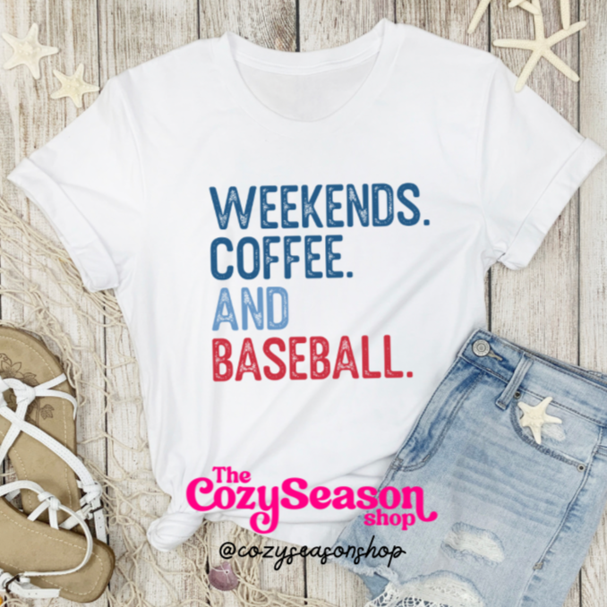 A white unisex adult t-shirt with the text 'WEEKENDS, COFFEE, AND BASEBALL' printed in red and blue colors, displayed on a wooden background with a pair of blue jeans, a pair of white sandals, and a decorative starfish.