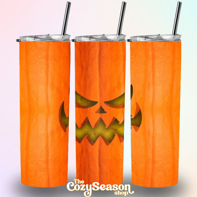 A 20oz travel tumbler with a stainless steel lid and a clear acrylic push-on lid tab, featuring a glitter print of a jack o lantern on an orange background. The tumbler is part of 'The Cozzy Season' shop collection.