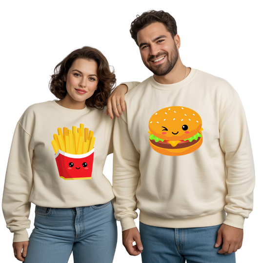 Two people wearing cream sweatshirts with cartoon food graphics (BURGER ON ONE SWEATSHIRT, FRIES ON THE OTHER) on a white background