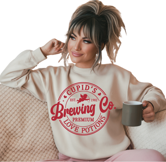 WOMAN WEARING A WHITE SWEATSHIRT WITH A BREWERY STYLE ROUND LOGO WITH THE TEXT: CUPID'S BREWING CO., PREMIUM LOVE POTIONS.