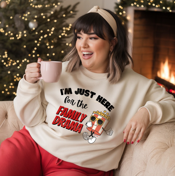 Woman wearing a sweatshirt with text and a graphic, sitting in front of a Christmas tree and fireplace.