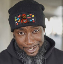 Man wearing a black beanie with a colorful patch and a dark hoodie.
