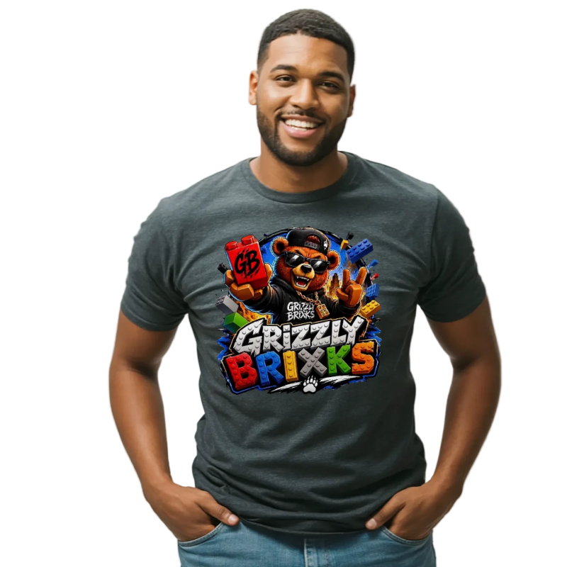 A man wearing a dark gray graphic t-shirt with a colorful 'Grizzly Brixks' bear design, paired with blue jeans, standing against a light gray studio background.