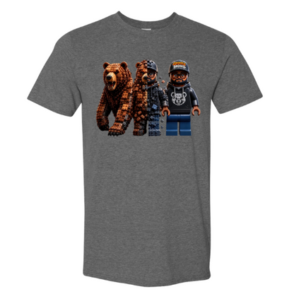 A heather gray short-sleeve crewneck t-shirt featuring a graphic print of three blocky, pixelated characters resembling Lego minifigures: a brown bear, a person in a dark jacket, and a person in a black hoodie and blue pants.