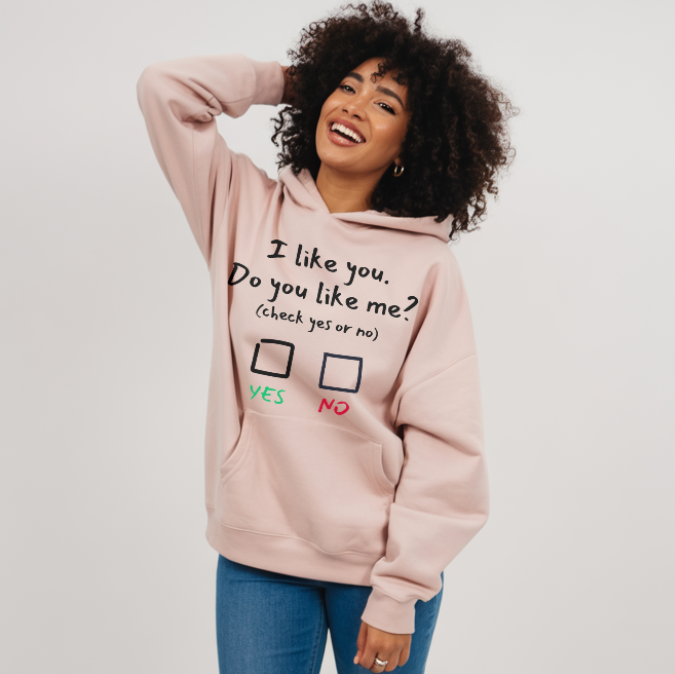 Person wearing a pink hoodie with a humorous question printed on it, standing against a plain background.