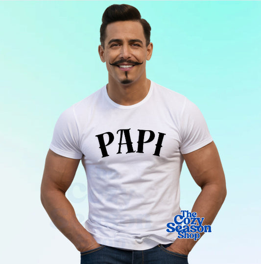 A man wearing a white t-shirt with the text 'PAPÍ' on the front, smiling with a mustache and glasses.