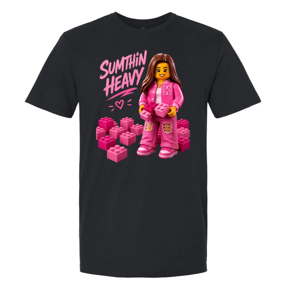 A black short-sleeve t-shirt with a graphic print on the front. The graphic features the text 'SUMTHIN HEAVY' in pink, a female LEGO minifigure wearing a pink outfit, and several pink building blocks.