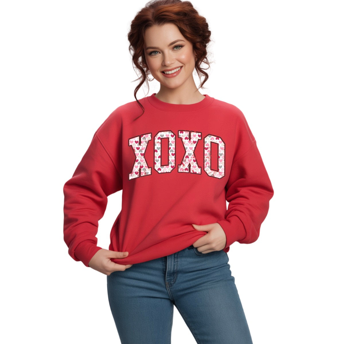 Woman wearing a red sweatshirt with 'XOXO' print on a white background. The XOXO design is in an upward arch with heart patterns inside the print. 