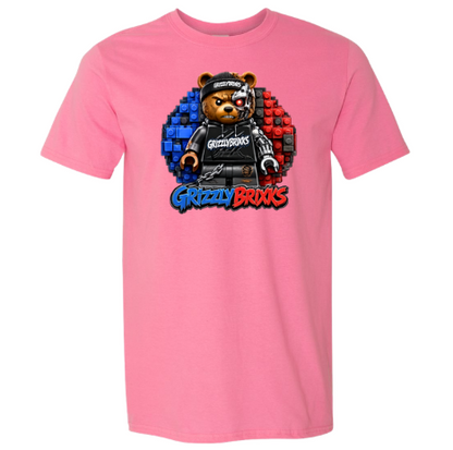 A pink short-sleeve crewneck t-shirt featuring a central graphic of a teddy bear wearing a black hoodie and cap, set against a blue and red pixelated circle, with the text 'Grizzly Brixks' below.