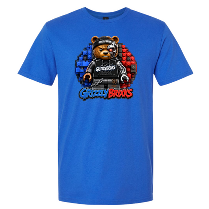 A royal blue short-sleeve t-shirt featuring a central graphic of a teddy bear wearing a black outfit and cap, set against a circular background split into blue and red brick patterns, with the text 'Grizzly Brixks' below.