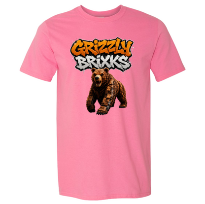 A pink short-sleeve crewneck t-shirt featuring a graphic print of a brown bear under the text 'Grizzly Brixks' in a graffiti-style font, displayed on a solid white background.