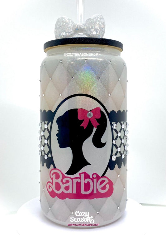 BARBIE THEME GLASS CAN CUP. The color is white with holographic flakes throughout. It is detailed with clear sparkling diamonds. Barbie's head silhouette sits in an oval frame. The Barbie logo is White and Hot Pink. The glass can has a bamboo lid that is painted in glossy black.